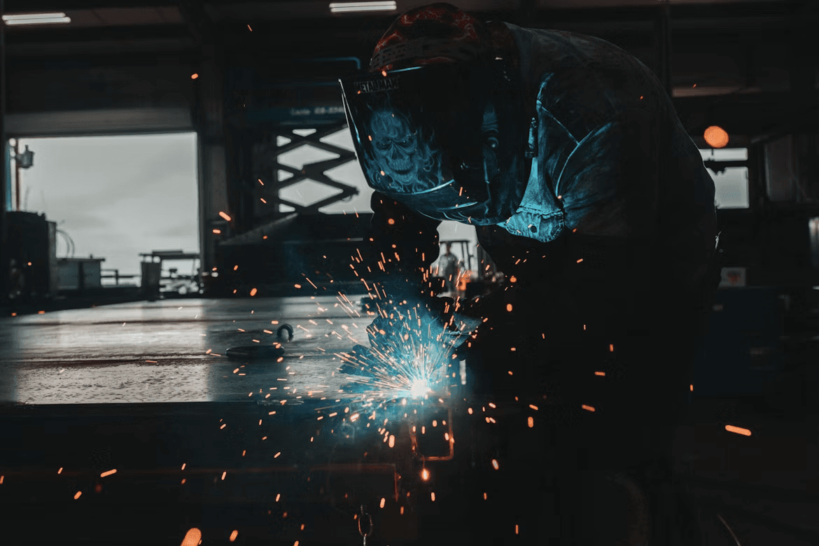 Welder fabricating steel in a workshop with a bright arc and flying sparks
