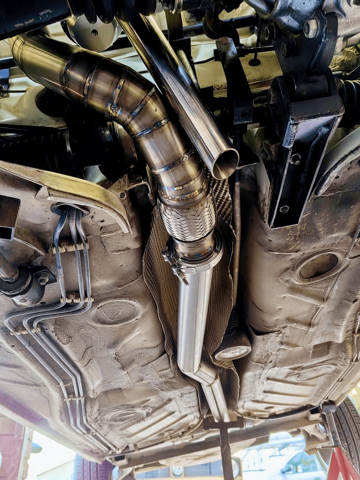 Custom stainless downpipe and exhaust section installed beneath a vehicle